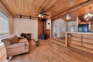 Living room with a wood stove, rail lighting, light wood-style floors, wood ceiling, and ceiling fan