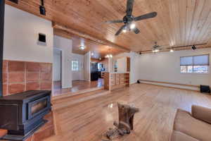 Unfurnished living room with rail lighting, wood ceiling, a wood stove, light wood-type flooring, and a ceiling fan