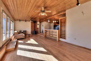 Living area with rail lighting, a wood stove, wooden ceiling, hardwood / wood-style flooring, and a ceiling fan