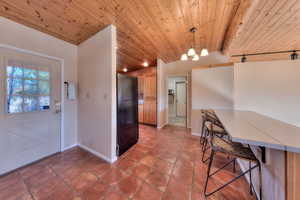 Kitchen featuring a kitchen bar, hanging light fixtures, freestanding refrigerator, wooden ceiling, and a chandelier