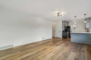 1597 - Kitchen featuring gray cabinetry, appliances with stainless steel finishes, pendant lighting, open floor plan, and light wood-style floors