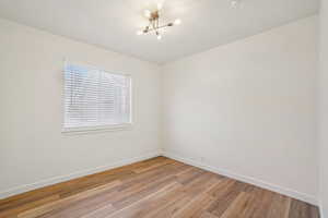 1597 - Unfurnished room featuring light wood-style flooring, a chandelier, and a smoke detector