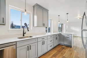 1597 - Kitchen with gray cabinets, hanging light fixtures, stainless steel dishwasher, light stone counters, and light wood-type flooring