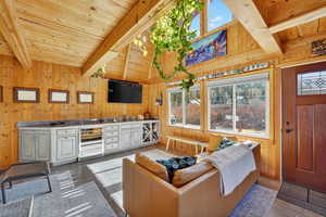 Living area with vaulted ceiling, wood walls, ample natural light and wine cooler