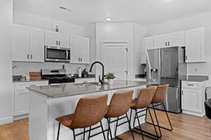 Kitchen with appliances with stainless steel finishes, white cabinets, a breakfast bar area, and a center island with sink
