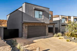 Contemporary home featuring stone siding, stucco siding, driveway, and an attached garage