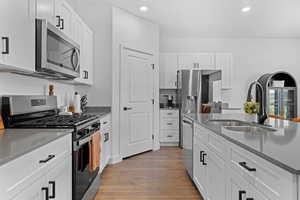 Kitchen with appliances with stainless steel finishes, white cabinets, light stone counters, light wood-style flooring, and recessed lighting