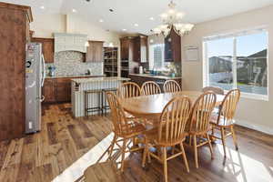 Dining room with dark wood-style floors, vaulted ceiling, a chandelier, and recessed lighting