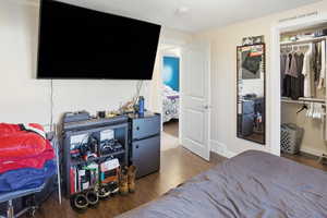 Bedroom with dark wood-style flooring, freestanding refrigerator, and a closet