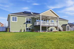 Rear view of property featuring ceiling fan, stairway, a wooden deck, a storage shed, and roof mounted solar panels
