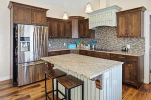 Kitchen with stainless steel refrigerator with ice dispenser, pendant lighting, a kitchen island, a kitchen bar, and decorative backsplash