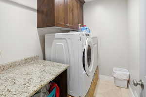 Laundry room featuring light tile patterned floors, separate washer and dryer, and cabinet space