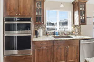Kitchen featuring glass insert cabinets, stainless steel appliances, light stone counters, and backsplash