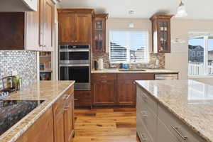 Kitchen with stainless steel appliances, backsplash, decorative light fixtures, glass insert cabinets, and light wood-style floors