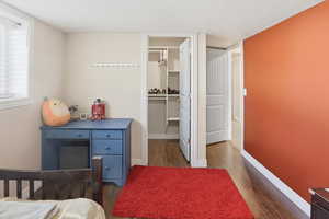 Bedroom with a textured ceiling, dark wood-style flooring, and a spacious closet