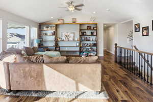 Living room featuring dark wood finished floors, lofted ceiling, ceiling fan, and built in features