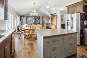 Kitchen featuring hanging light fixtures, appliances with stainless steel finishes, lofted ceiling, open floor plan, and dark wood finished floors
