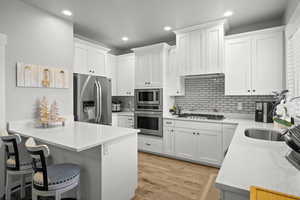 Kitchen featuring stainless steel appliances, light stone countertops, white cabinets, a breakfast bar, and light wood-style floors