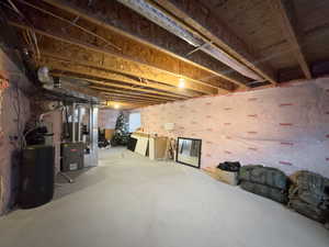 Unfinished below grade area featuring a water softener and heating unit