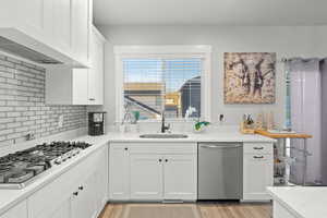 Kitchen featuring white cabinets, stainless steel appliances, range hood, light stone countertops, and light wood-style floors