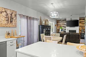 Kitchen with a fireplace, dishwasher, hanging light fixtures, light stone countertops, and white cabinetry