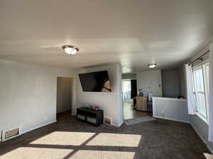 Unfurnished living room featuring dark colored carpet and baseboards