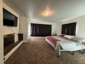 Carpeted Master bedroom featuring a brick fireplace, a textured ceiling, and a textured wall. Could also be used as a family room.