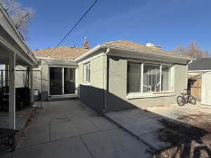 Rear view of property featuring a patio, roof with shingles, brick siding, and a chimney