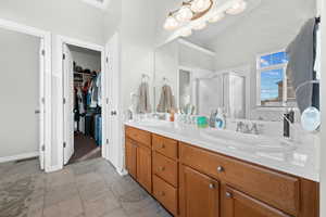 Bathroom featuring double vanity, light tile finish floors, a shower stall, and a spacious closet