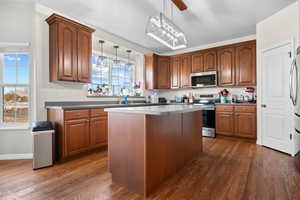 Kitchen with appliances with stainless steel finishes, wood cabinets, dark wood-type flooring, and a center island