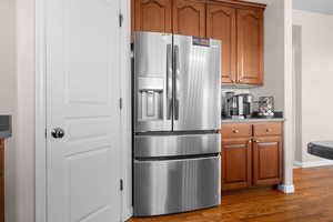 Kitchen with stainless steel refrigerator with ice dispenser, brown cabinets, dark wood-style flooring, and light stone counters