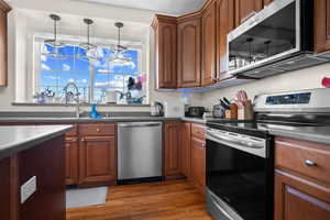 Kitchen with stainless steel appliances, dark wood-style floors, dark countertops, and hanging light fixtures