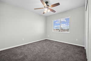 Spare room featuring dark colored carpet and a ceiling fan