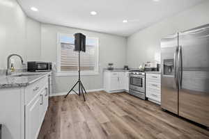 Kitchen featuring appliances with stainless steel finishes, white cabinets, light stone countertops, light wood-style floors, and recessed lighting