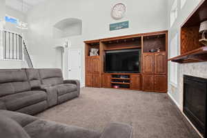 Carpeted living room featuring a towering ceiling, stairway, a healthy amount of natural light, and the view of the entrance to the primary bedroom.