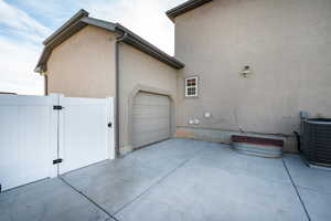 View of side of property featuring a gate, stucco siding, concrete driveway, and an attached garage