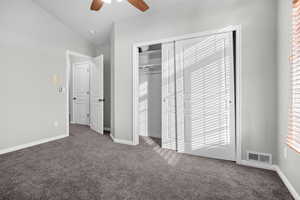 Unfurnished bedroom featuring dark colored carpet, vaulted ceiling, ceiling fan, multiple windows, and a closet