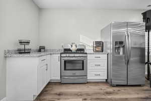Basement kitchen with white cabinetry, stainless steel appliances, light stone counters, and light wood-type flooring