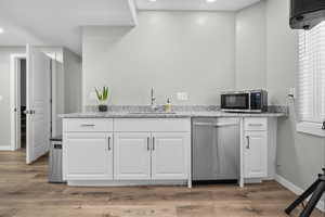 Basement kitchen featuring white cabinetry, stainless steel appliances, light stone countertops, light wood-type flooring, and recessed lighting
