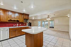 Kitchen featuring brown cabinetry, stainless steel appliances, light countertops, open floor plan, and a ceiling fan