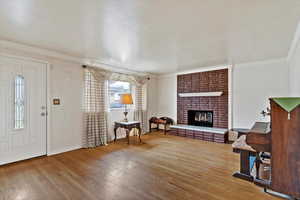 Entryway with a brick fireplace, ornamental molding, and light wood finished floors