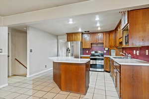 Kitchen with stainless steel appliances, light countertops, brown cabinetry, a center island, and recessed lighting