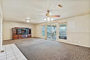 Unfurnished living room with a textured ceiling, ceiling fan, carpet floors, and tile patterned floors