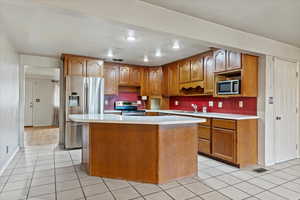 Kitchen featuring stainless steel appliances, light countertops, brown cabinets, light tile patterned floors, and recessed lighting