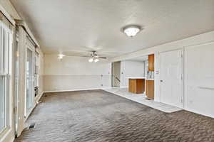Unfurnished room featuring a textured ceiling, light carpet, and a ceiling fan