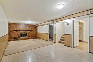 Finished below grade area with wainscoting, a textured ceiling, wood walls, a brick fireplace, and stairway