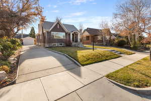 View of front of property featuring a detached garage, an outbuilding, brick siding, a front yard, and concrete driveway