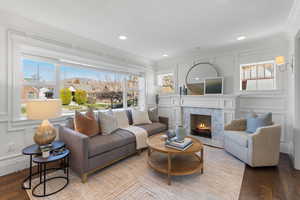 Living room featuring a decorative wall, crown molding, a premium fireplace, wood finished floors, and recessed lighting