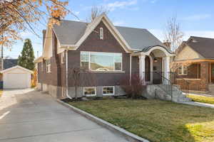 View of front of house with brick siding, an outdoor structure, a front yard, and a garage