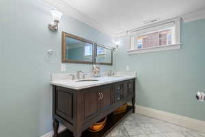 Bathroom featuring double vanity, ornamental molding, plenty of natural light, and light marble finish flooring